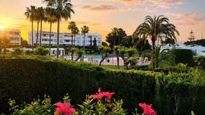 A resort with a pool, palm trees, and a building with balconies. - Sunny Garden Apartment Miraflores (Mijas Costa)