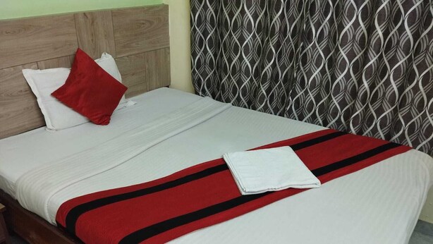 A neatly made bed with a white and red striped blanket, a red pillow, and a white towel. - Welcome Regency (Barasat)