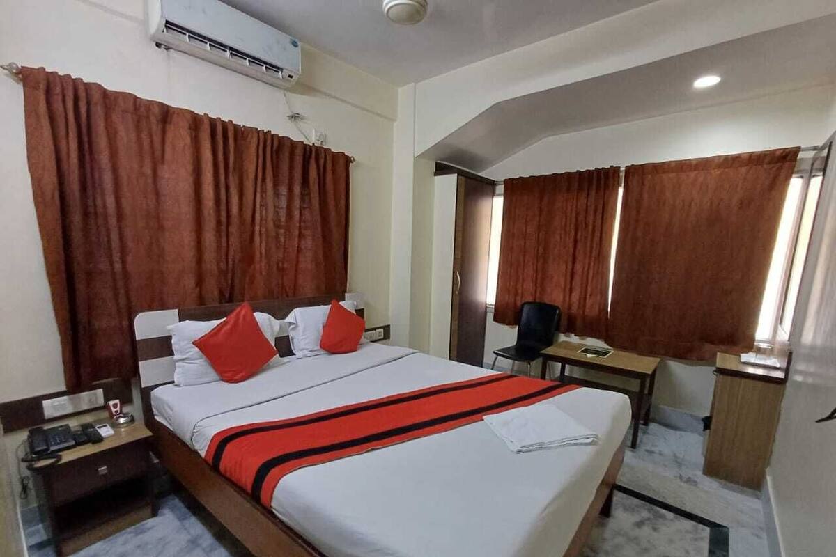 A hotel room with a bed, a desk, a chair, and an air conditioning unit.