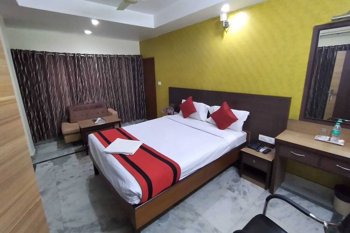 A hotel room with a bed, a desk, a chair, a nightstand, a ceiling fan, and a mirror.