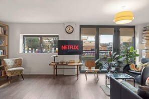 A living room with a television displaying 'NETFLIX', a chessboard, a clock, and a bookshelf. - Canal-view London Flat Near Victoria Park (London)