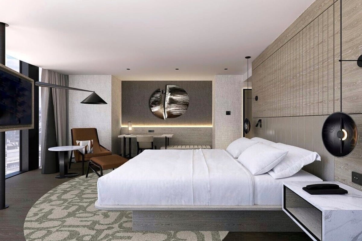 Une chambre d’hôtel moderne équipée d’un grand lit, d’une télévision, d’un bureau, d’une chaise et d’un luminaire fixé au mur.