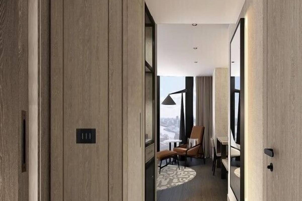 Un couloir d’hôtel moderne avec des panneaux de bois, un coin salon avec une table et des chaises, et une vue par la fenêtre.