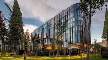 Edifício moderno com fachada de vidro, cercado por árvores e um gramado bem cuidado.