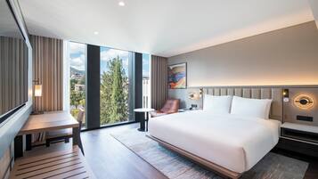 Quarto de hotel moderno com uma cama grande, uma escrivaninha, uma cadeira e vista para o exterior.