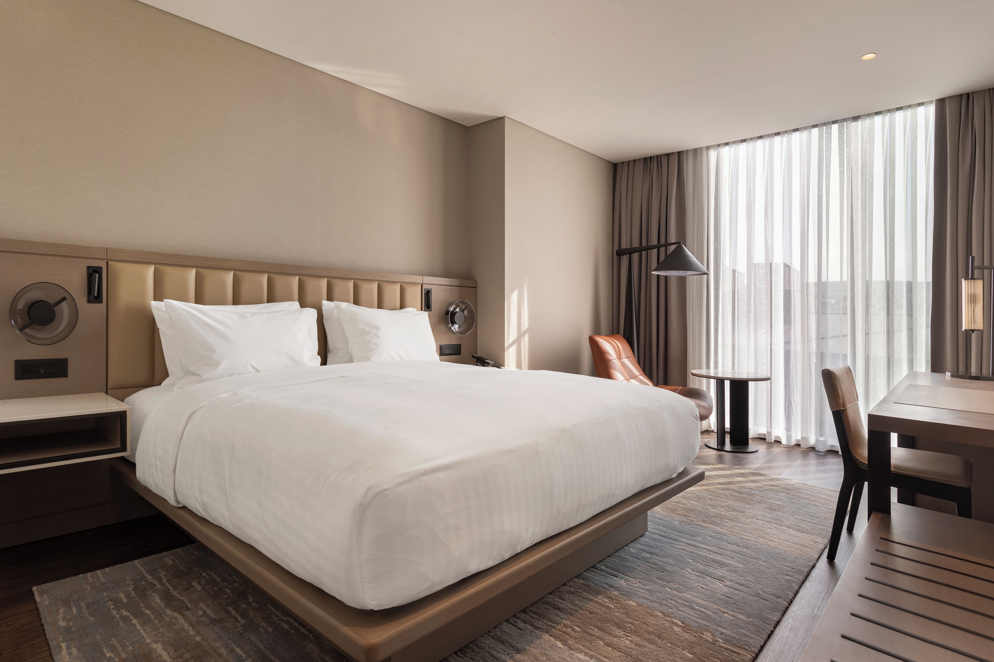 A hotel room with a large bed, a desk, a chair, and a window with curtains.