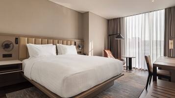 A hotel room with a large bed, a desk, a chair, and a window with curtains.