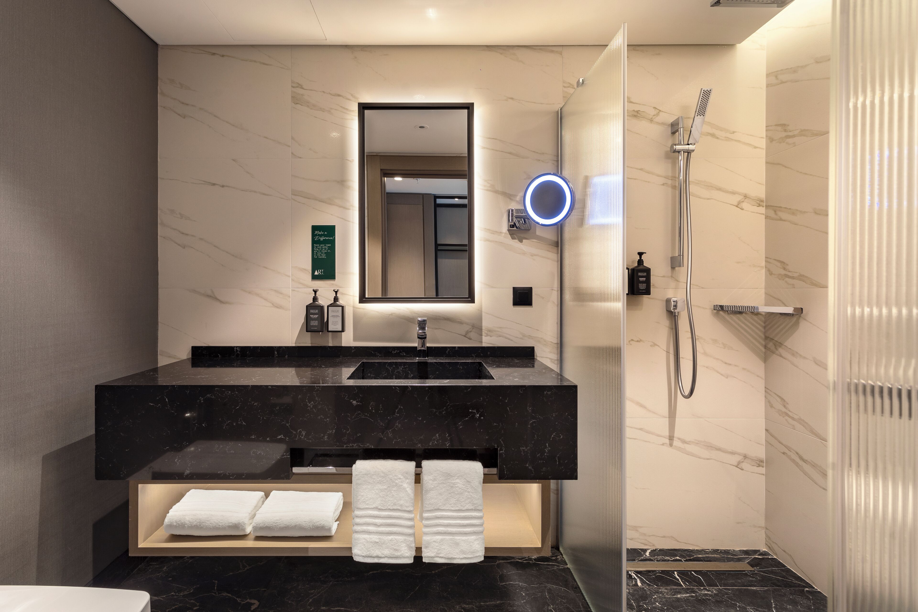 A modern bathroom with a black marble vanity, a large mirror, and a glass-enclosed shower.