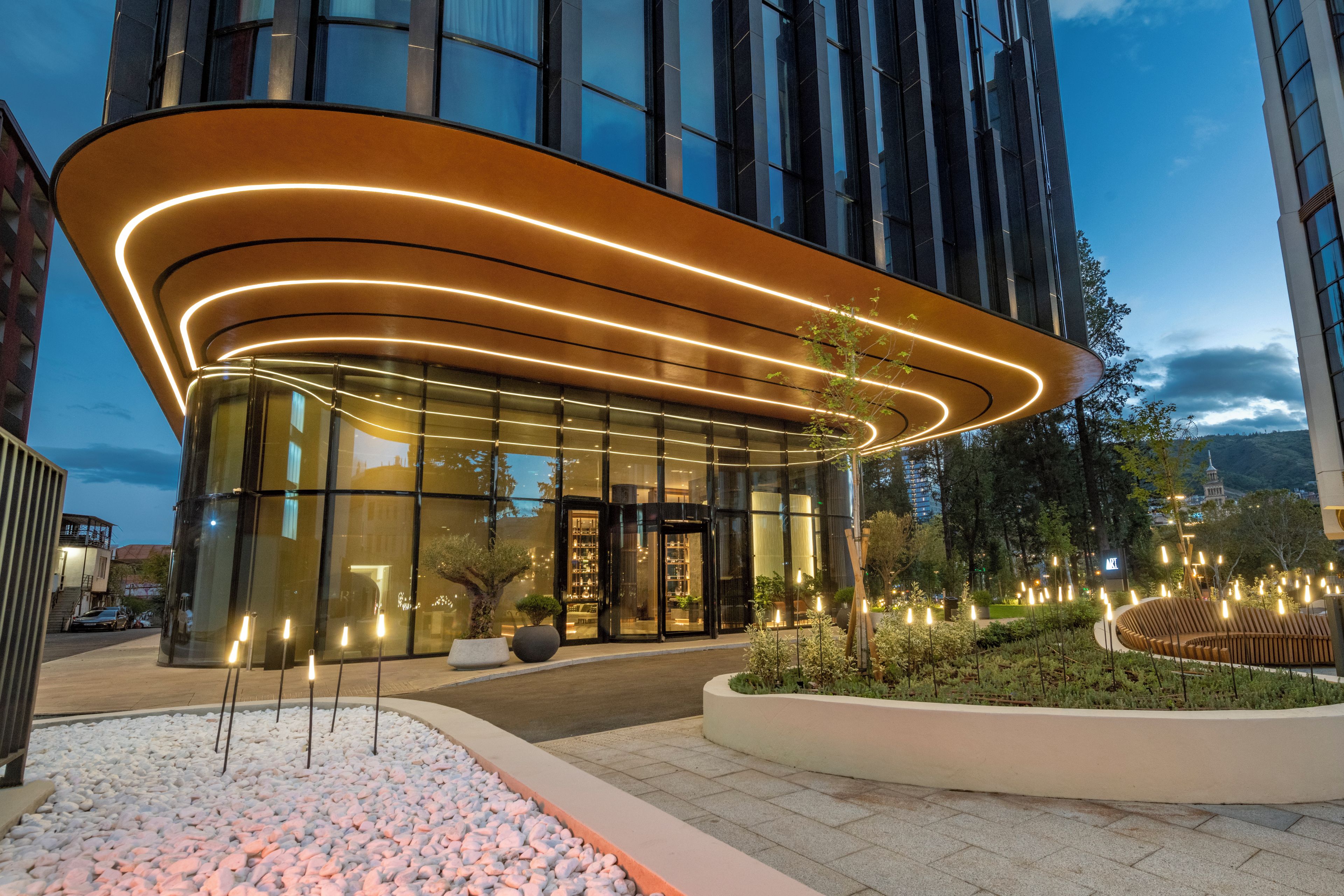 A modern building with a curved entrance, glass facade, and outdoor seating area with plants.