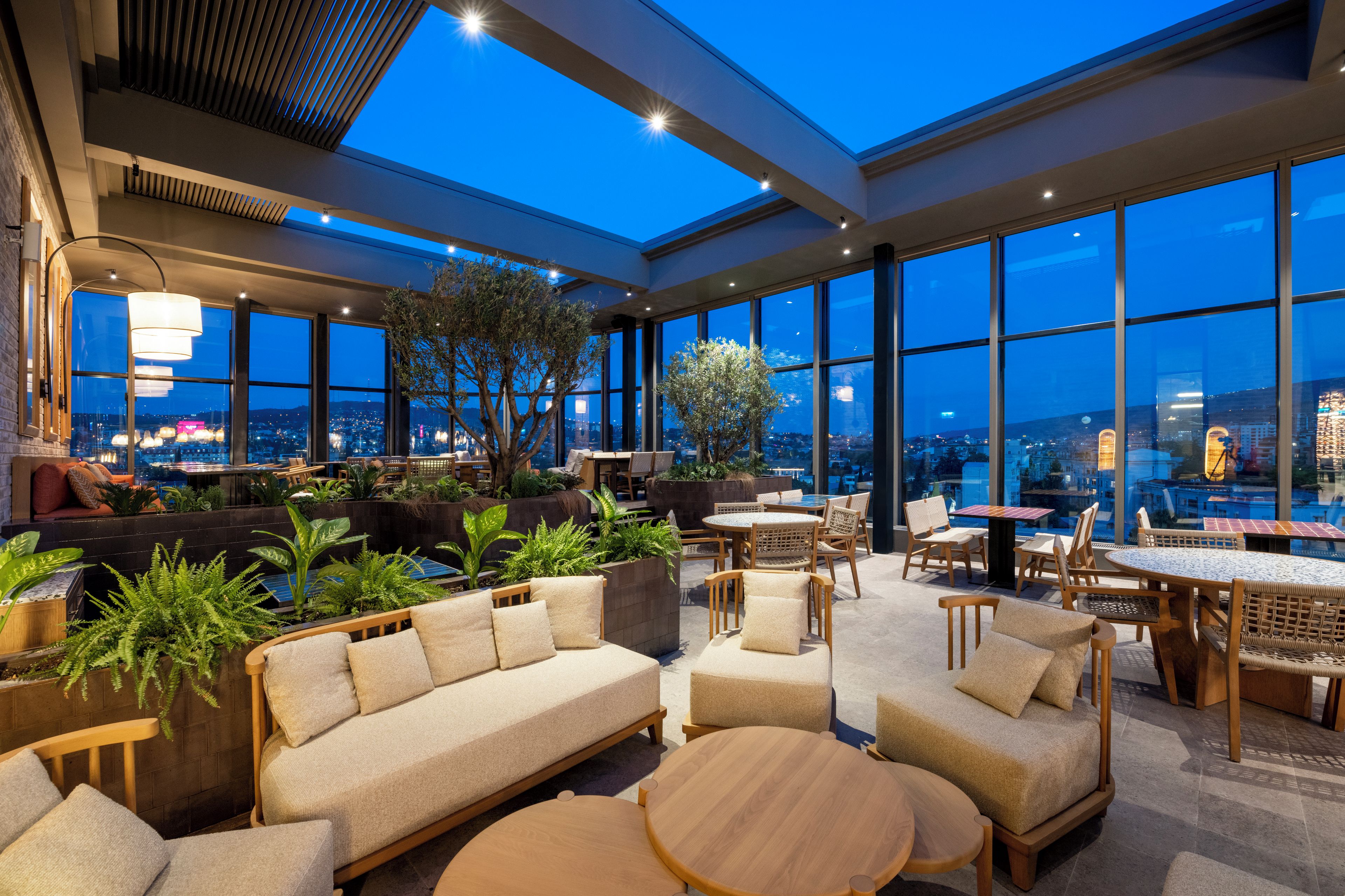 A spacious indoor area with seating arrangements, large windows, and a view of the cityscape.
