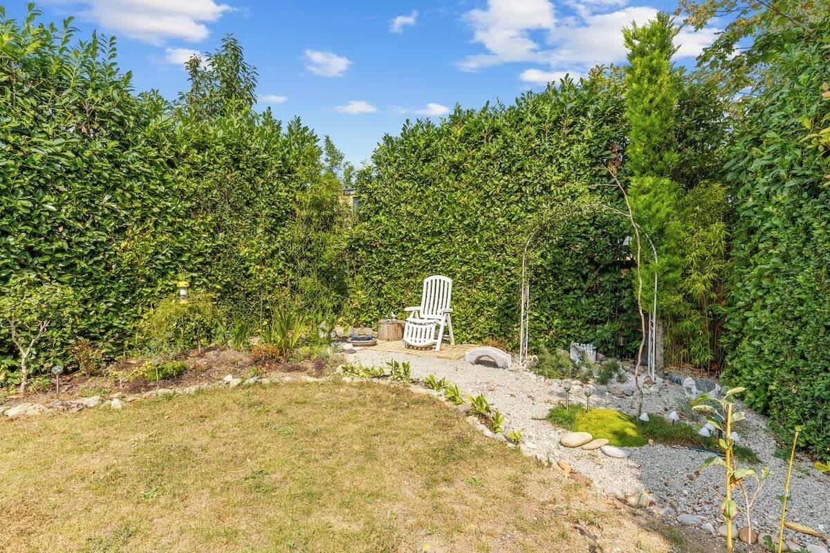 A garden with a white chair, dense foliage, and a clear sky.
