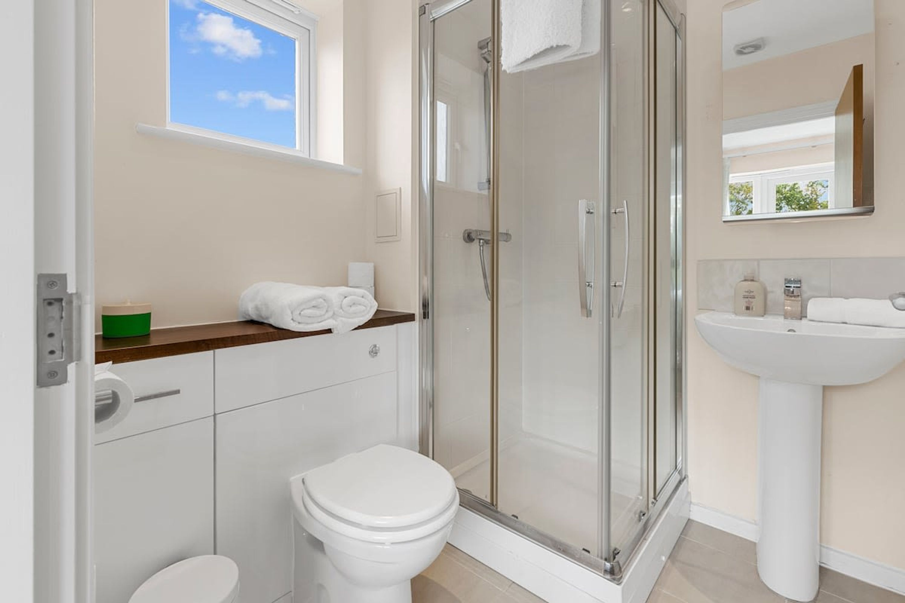 A modern bathroom with a toilet, a glass-enclosed shower, a sink, and a window.