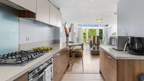 A modern kitchen with a gas stove, oven, and microwave. There is a dining area with a table and chairs. - 3-bed Greenhithe Retreat Garden Near Bluewater (Greenhithe)