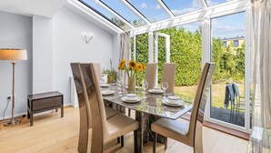 A dining area with a glass table, chairs, and a view of greenery outside. - 3-bed Greenhithe Retreat Garden Near Bluewater (Greenhithe)