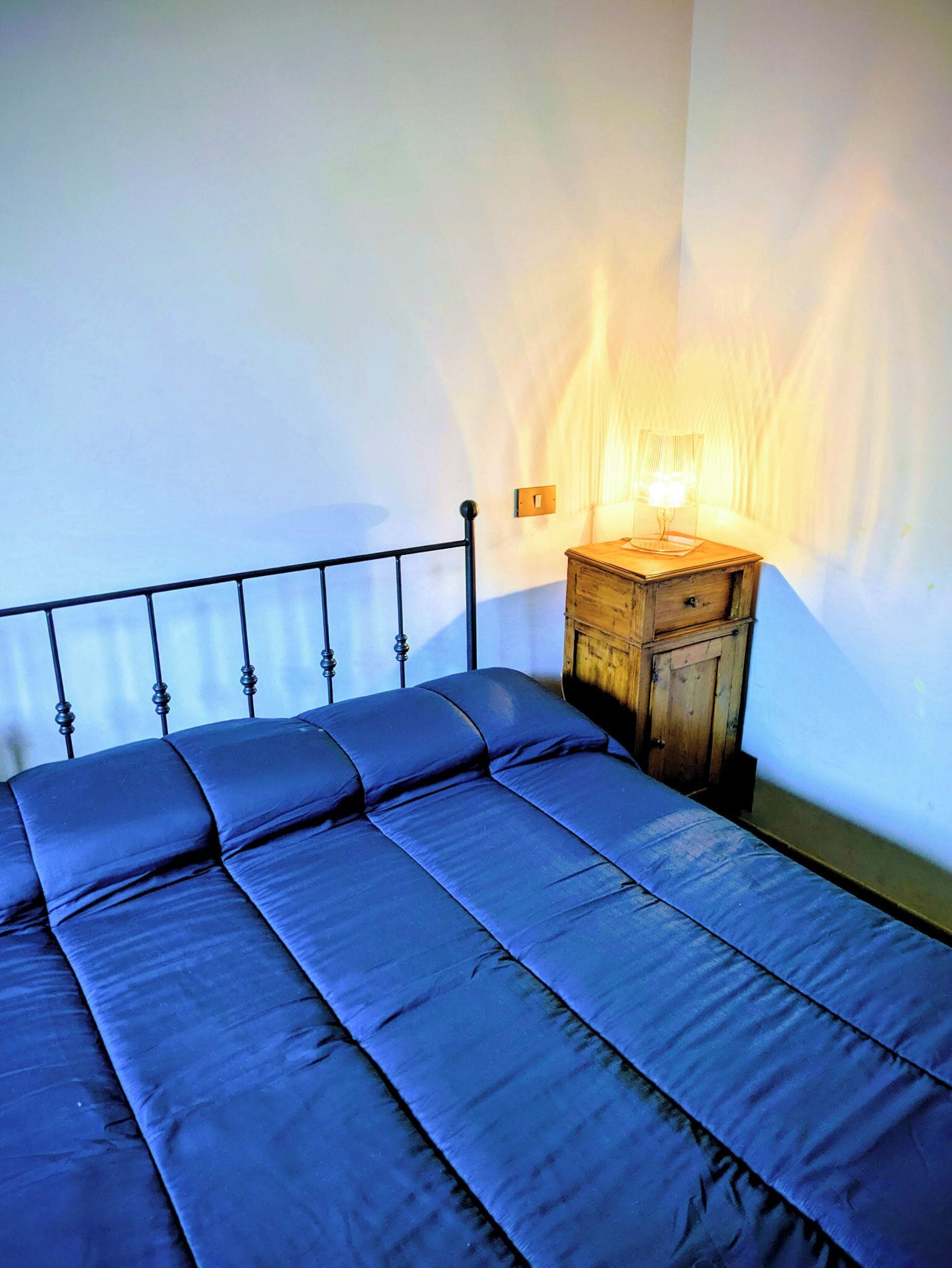 Un letto con struttura in metallo e un comodino in legno con una lampada.