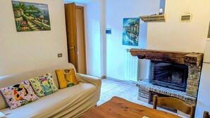 A living room with a white sofa, colorful cushions, a wooden coffee table, a stone fireplace, and two paintings on the walls. - Lucoli Antico (Lucoli)