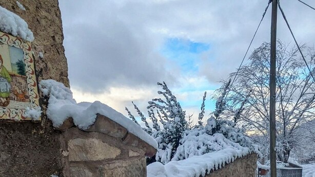 A stone wall with a small water channel, surrounded by snow-covered trees and a cloudy sky. - Lucoli Antico (Lucoli)