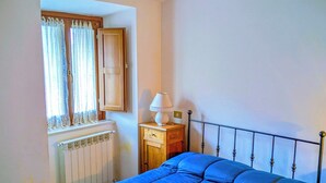 A bedroom with a bed, a window with curtains, a radiator, and a bedside table with a lamp. - Lucoli Antico (Lucoli)