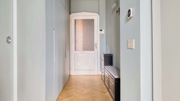 A narrow hallway with a wooden herringbone floor, a white door with a textured glass panel, and a small black cabinet against the wall. - w Bright 2BR Near Arco Della Pace (Milan)