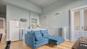 A modern living room with a blue sectional sofa, a white refrigerator, and a wooden herringbone floor. - w Bright 2BR Near Arco Della Pace (Milan)