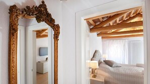 A bedroom with a wooden ceiling, a large ornate mirror, a bed with a grey duvet, and a bedside table with a lamp. - Address: Calle de le Ancore, 1044 - Castello BiennaleGoogle maps ' position: https://maps.app.goo.gl/ZF2iGXAu1hQr4UdG7The apartment is located on the third floor, consisting of a bedroom, bathroom with tub, living room with sofa bed for 2 people, kitchen (Venezia)