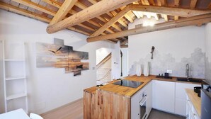 A compact kitchen with a wooden island, white cabinetry, and a visible staircase leading to an upper level. - Address: Calle de le Ancore, 1044 - Castello BiennaleGoogle maps ' position: https://maps.app.goo.gl/ZF2iGXAu1hQr4UdG7The apartment is located on the third floor, consisting of a bedroom, bathroom with tub, living room with sofa bed for 2 people, kitchen (Venezia)