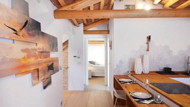 A modern kitchen with wooden beams, a dining table set for two, and artwork on the walls. - Address: Calle de le Ancore, 1044 - Castello BiennaleGoogle maps ' position: https://maps.app.goo.gl/ZF2iGXAu1hQr4UdG7The apartment is located on the third floor, consisting of a bedroom, bathroom with tub, living room with sofa bed for 2 people, kitchen (Venezia)