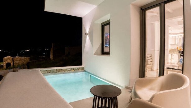 Et moderne poolområde udendørs med minimalistisk design, et lille rundt bord og behagelige siddepladser.