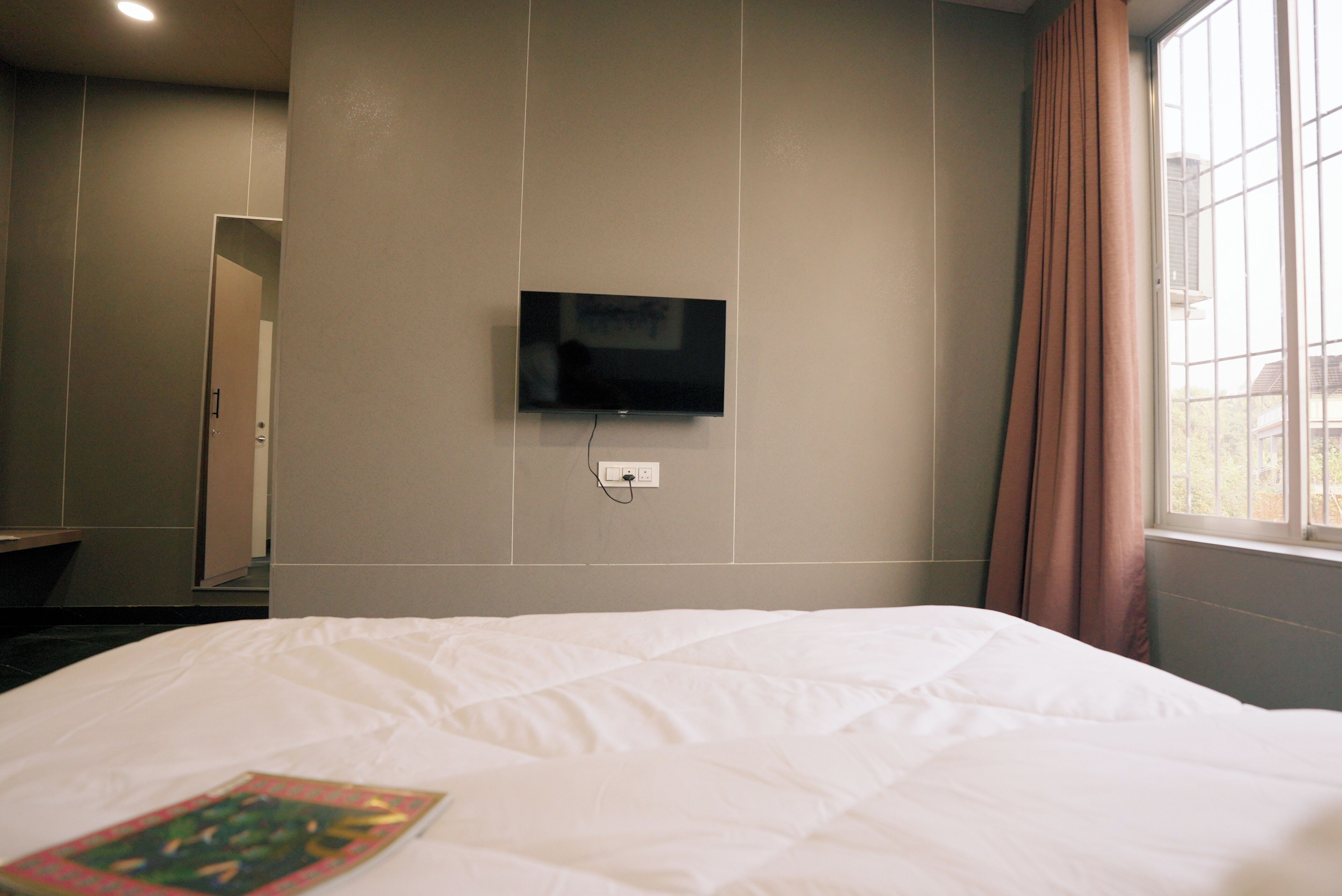 A hotel room with a bed, a television mounted on the wall, and a window with curtains.