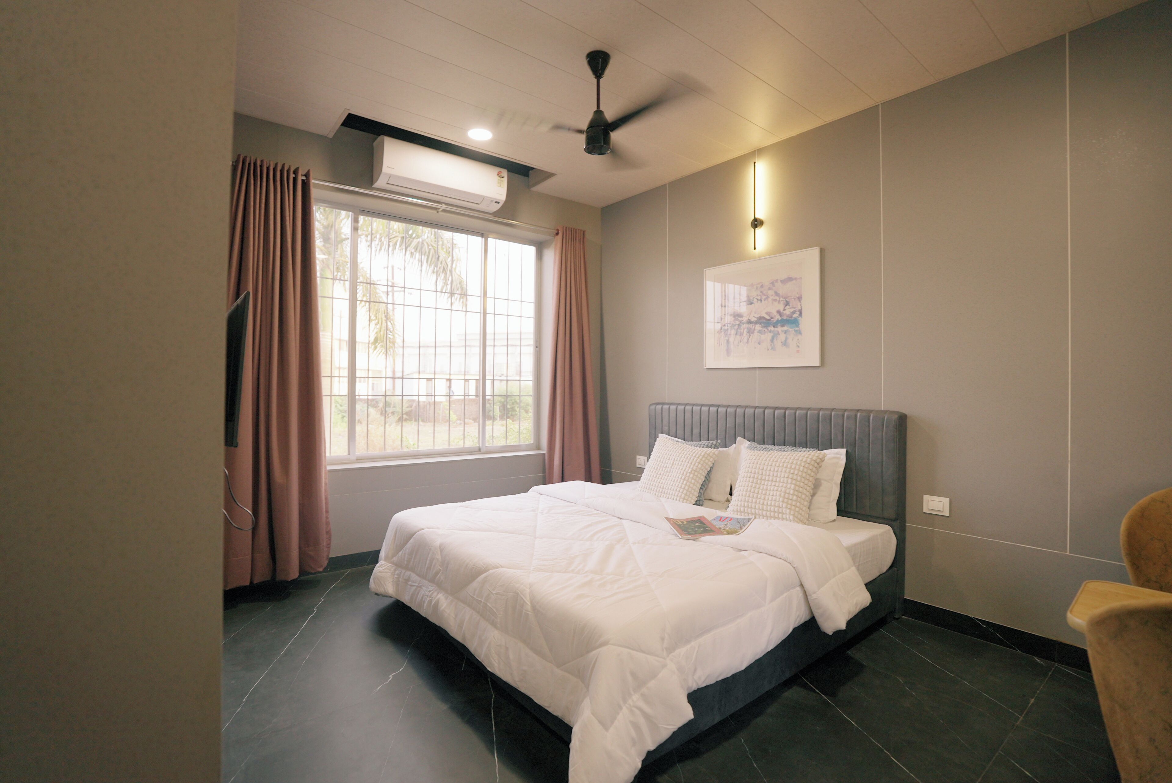 Een slaapkamer met een bed, een plafondventilator, een raam met gordijnen en een wandlamp.