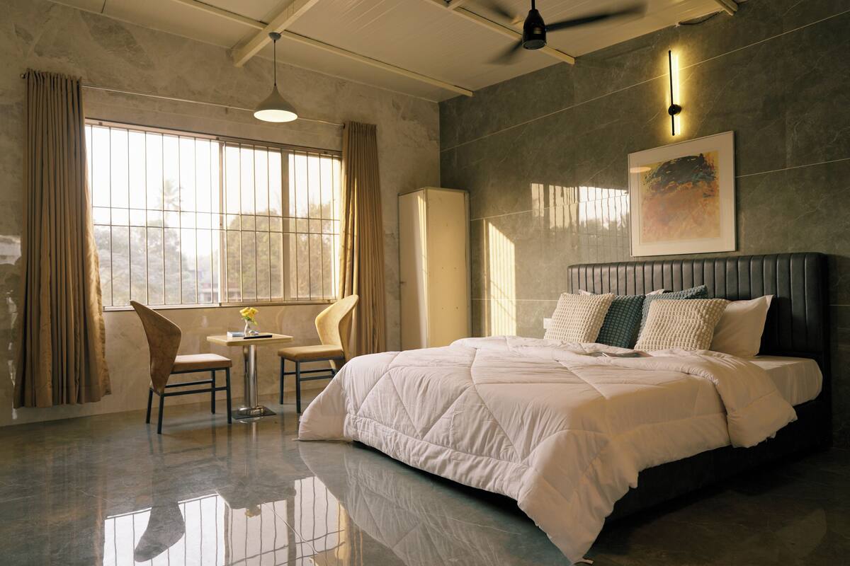 A bedroom with a large bed, a chair, a small table, and a window with curtains.