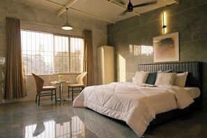 Ein Schlafzimmer mit einem großen Bett, einem Sessel, einem kleinen Tisch und einem Fenster mit Vorhängen.