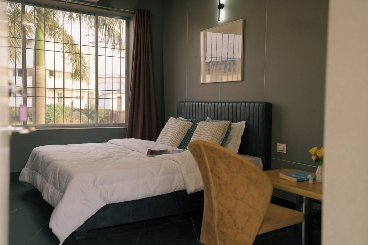 A bedroom with a bed, a chair, a desk, and a window with curtains.