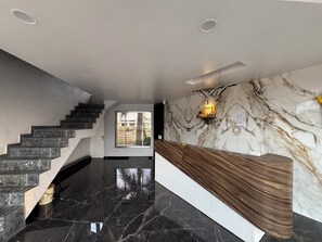 Una hall moderna di un hotel, con una reception in marmo, una scala e vista sull'esterno.