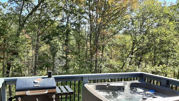 A hot tub on a wooden deck with a barbecue grill nearby, surrounded by trees. - Kettlestone (Stanton)