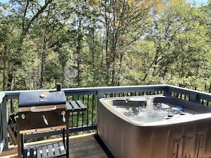 A hot tub on a wooden deck with a barbecue grill nearby, surrounded by trees. - Kettlestone (Stanton)