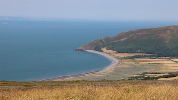A coastal landscape with a curved shoreline, fields, and distant hills.