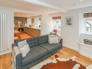 A modern living room with a grey sofa, a cowhide rug, and a kitchen in the background. - The Old Workshop (Dulverton)