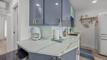 A kitchen with a white marble countertop, a coffee maker, and a sink.