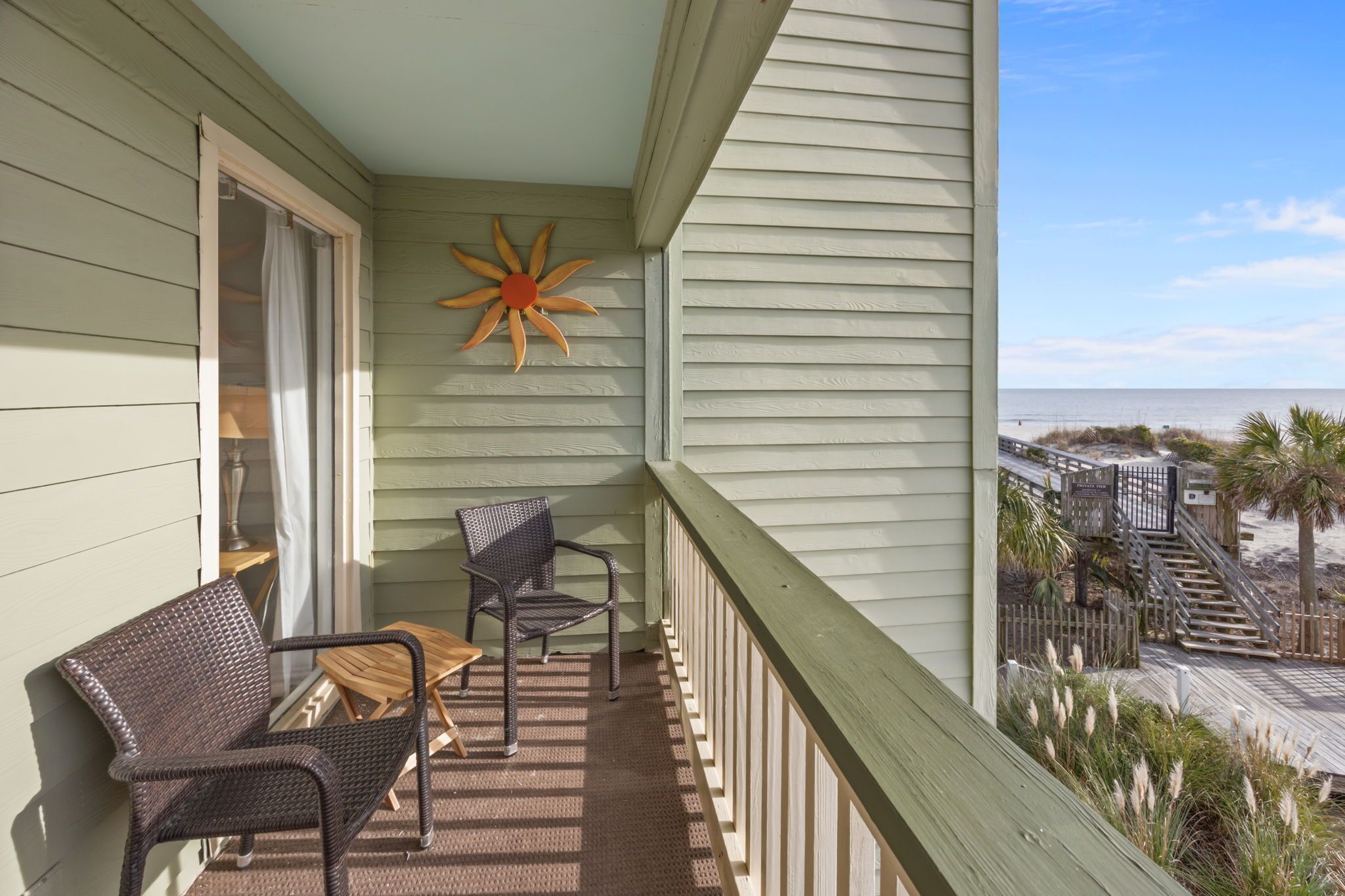 A balcony with wicker furniture, a wooden chair, and a decorative sun-shaped object.