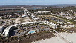 Vue aérienne d’un hôtel situé sur la côte, avec une piscine, des aires de stationnement et un pont d’accès à la plage.