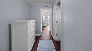 Un couloir avec une commode blanche, un tapis bleu et une porte donnant sur une autre pièce.