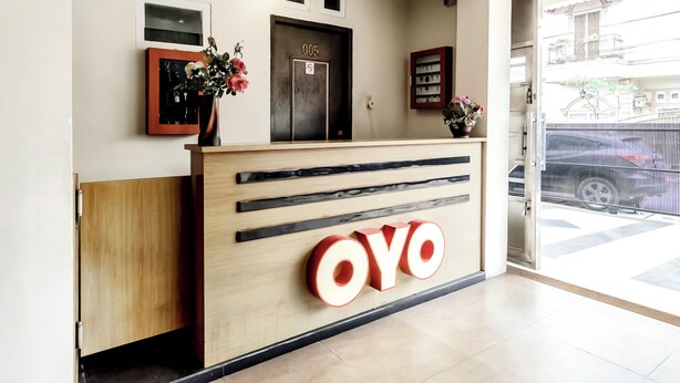 A reception desk with the name "OYO" prominently displayed, a framed photo above the door, and a small potted plant to the left. - Collection O 294 Andrea Residence (Medan)