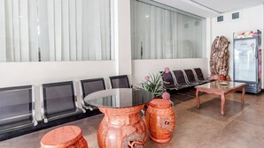 A waiting area with a glass-top table, several chairs, a refrigerator, and a decorative plant. - Collection O 294 Andrea Residence (Medan)