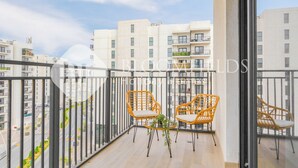 A balcony with two wicker chairs and a small table, overlooking a cityscape with modern buildings. - Bloomfields Modern 1Br Water's edge (Abu Dhabi)