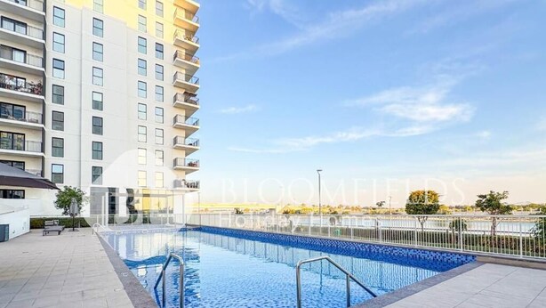A swimming pool with a tiled deck, surrounded by a high-rise building with balconies. - Bloomfields Modern 1Br Water's edge (Abu Dhabi)