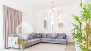 A modern living room with a grey sectional sofa, a white rug, a large mirror, and a bamboo plant. - Bloomfields Modern 1Br Water's edge (Abu Dhabi)