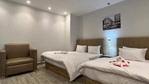 Ett hotellrum med två sängar, en soffa och en väggmonterad lampa.