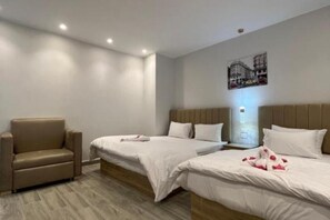 A hotel room with two beds, a sofa, and a wall-mounted light fixture.