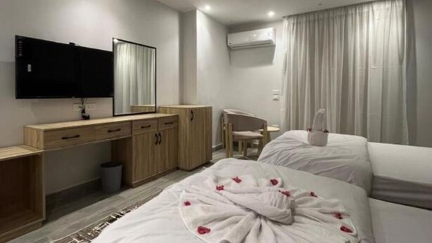 Ett hotellrum med en säng, ett skrivbord, en stol, en tv och ett fönster med gardiner.